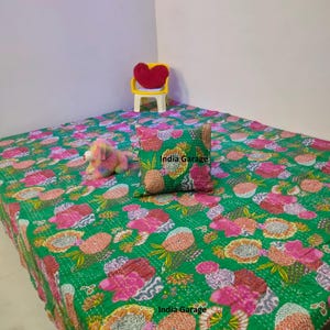 Könnte beinhalten: Eine grüne Steppdecke mit Blumenmuster in Rosa und Orange, ein passendes Kissen und ein kleiner gelber Stuhl mit einem herzförmigen roten Kissen. Der Text "India Garage" ist auf der Steppdecke und dem Kissen zu sehen.