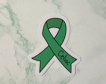 Könnte beinhalten: Ein grüner Aufkleber in Form eines Awareness-Ribbons mit dem Wort "Celiac" in handschriftlicher Schrift. Das Band ist hellgrün mit schwarzer Umrandung und weißem Rand. Der Aufkleber befindet sich auf einem weiß-grünen Marmorhintergrund.