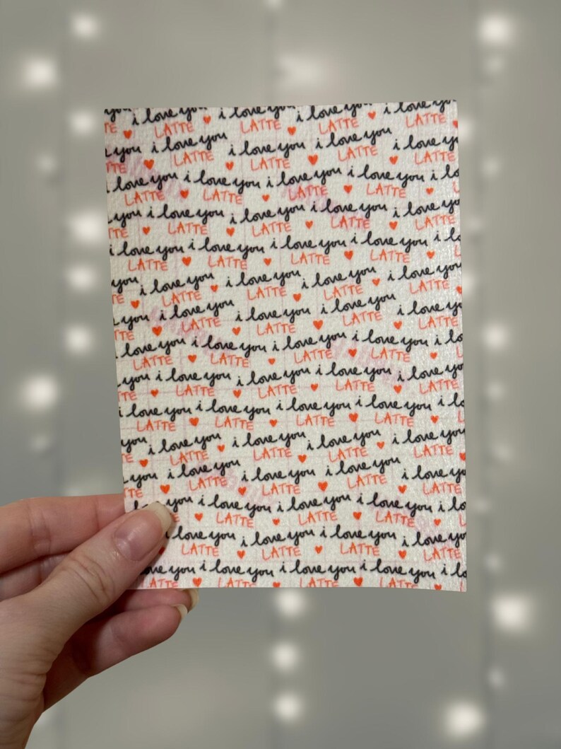 Puede incluir: Una tela blanca con un patr&oacute;n repetido de las palabras "Te amo" y "Latte" en escritura negra con peque&ntilde;os corazones rojos.