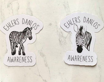 May include: Two white stickers with a zebra illustration and the text "Ehlers Danlos Awareness". One sticker shows a full zebra, the other a zebra's head. The zebra has black and white stripes.