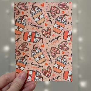 Puede incluir: Tela rosa con un patr&oacute;n repetido de tazas de caf&eacute; con crema batida y pajitas, corazones y el texto "I love you latte".