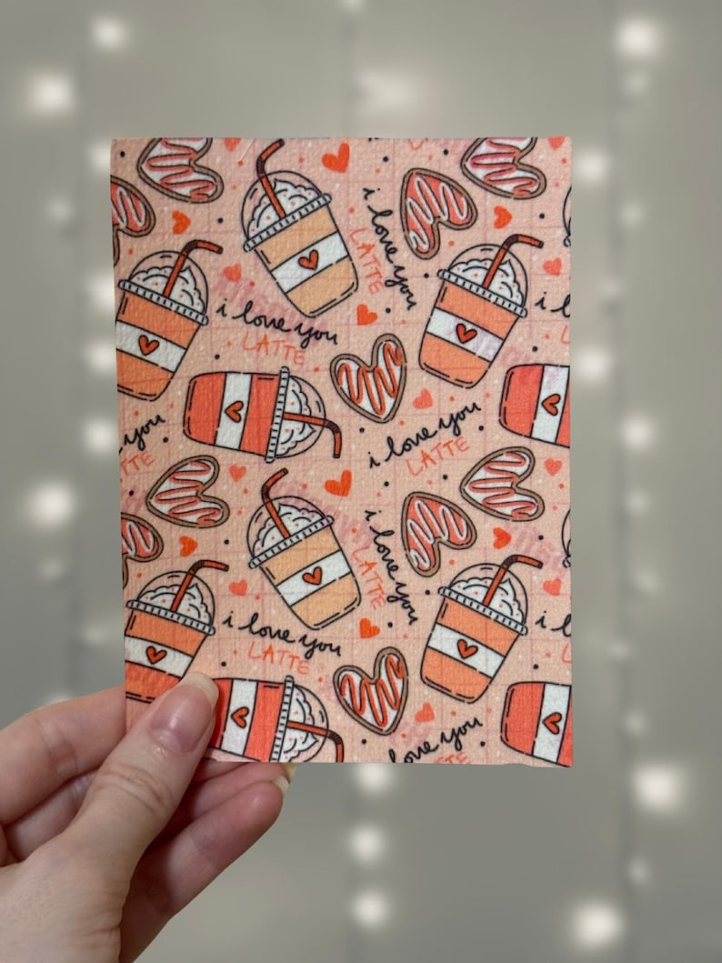 Puede incluir: Tela rosa con un patr&oacute;n repetido de tazas de caf&eacute; con crema batida y pajitas, corazones y el texto "I love you latte".