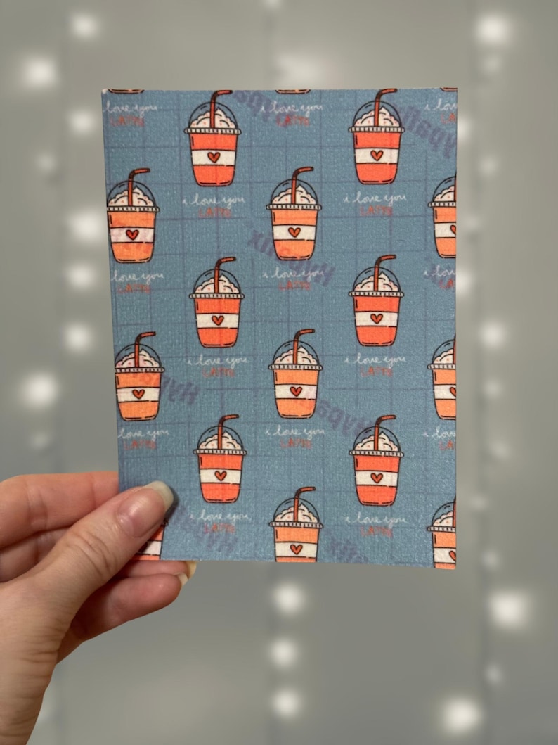 Puede incluir: Una tarjeta con un patr&oacute;n azul y blanco con un patr&oacute;n repetido de vasos de caf&eacute; helado naranja y blanco con un coraz&oacute;n en el lateral. El texto "Te amo" se repite en todo el patr&oacute;n.