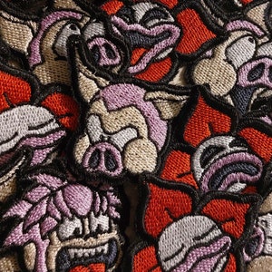 May include: A close-up of several embroidered patches featuring a cartoon pig with a pink snout and black eyes. The patches are on a red, black, and white background.