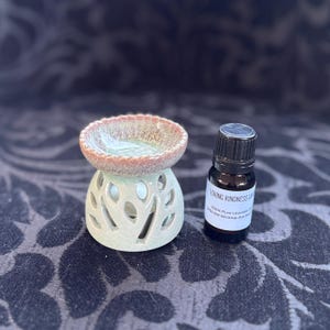 May include: A ceramic oil diffuser with a tree design in a light green and brown glaze. A small bottle of essential oil is next to the diffuser. The bottle label reads "Loving Kindness Lavender Oil 100% Pure Lavender Oil 1024 SW Wickiup Ave #100 Phoenix, AZ 85041".