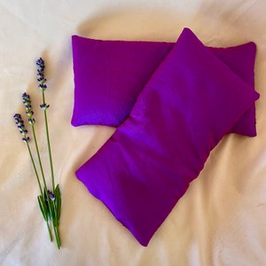 May include: Two purple fabric eye pillows, one on top of the other, on a white background.