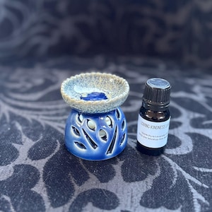 May include: Blue and white ceramic oil diffuser with a small bottle of essential oil. The bottle label reads "Loving Kindness Lavender 100% Pure Lavender Oil 320 SW Wicklup Ave, Bend, OR 97702".