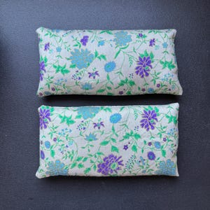 May include: Two rectangular pillows with a white background and a floral pattern in shades of green, blue, and purple.