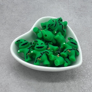 May include: A bowl of green and black silicone beads shaped like a character from a popular Halloween movie. The beads are designed to be used for jewelry making or other crafts.
