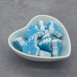 May include: A heart-shaped white bowl filled with blue and white castle-shaped beads. The beads have a light blue castle design on a white base. The beads are small and appear to be made of a hard material.
