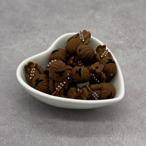 May include: A white heart-shaped dish filled with brown silicone charms shaped like the Star Wars character Chewbacca.