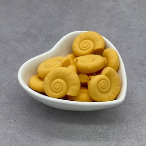 Può includere: Una ciotola bianca a forma di cuore piena di morsi di silicone gialli a forma di conchiglia.