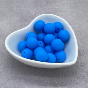 May include: A white heart-shaped bowl filled with bright blue silicone beads. The beads are smooth and round, perfect for sensory play or crafting.