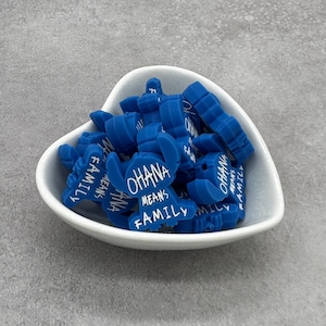 May include: A bowl filled with blue silicone charms shaped like a crab. Each charm has the text "Ohana means family" written on it.