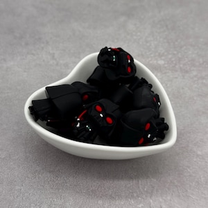 Könnte beinhalten: Eine weiße herzförmige Schale gefüllt mit schwarzen und roten Gummianhängern in Form von Darth Vader.