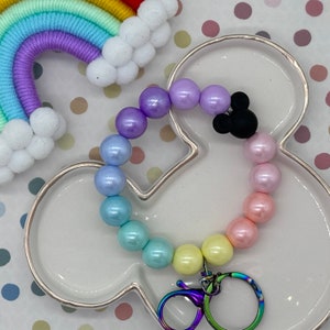 May include: A rainbow-colored beaded keychain with a black Mickey Mouse charm and a silver swivel clasp. The keychain is on a white background with polka dots.