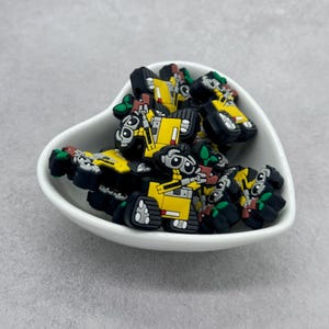 May include: A collection of small, yellow robot figurines with black and green details. The robots are in a white heart-shaped dish.