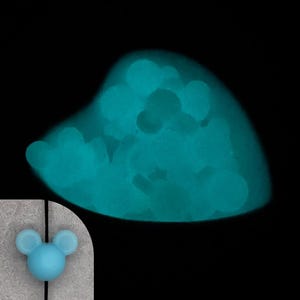 May include: A glowing, teal-colored heart-shaped object against a black background. The heart is filled with smaller, round shapes. A small, light blue Mickey Mouse head is in the lower left corner.