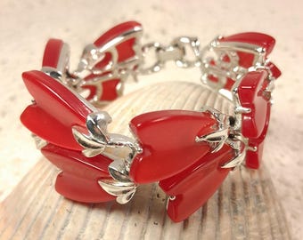 May include: A red bracelet with a silver-tone metal chain and accents. The bracelet features red, petal-shaped links connected by silver-tone metal links. The bracelet is displayed on a seashell.