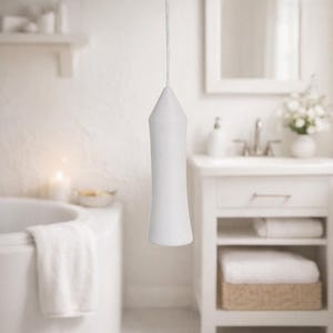 May include: A matte white, elongated, tapered light pull handle with a smooth, curved silhouette. The handle is suspended from a white braided cord, featuring a pointed top and a wider, flat base, designed for operating a ceiling light switch.