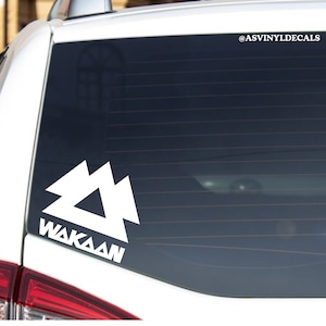 May include: White vinyl decal with a stylized mountain design and the word "WAKASAN" below it. The decal is on the back window of a car. The decal is for sale on Etsy.