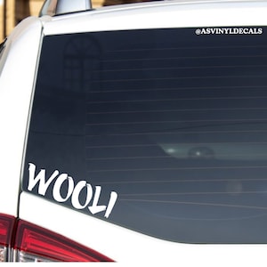 May include: White vinyl decal with the word "WOOLI" written in a stylized font with an arrow pointing down. The decal is on the back window of a white car.