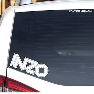 May include: White vinyl decal with the word "INZO" in a bold, stylized font. The decal is applied to the rear window of a white car. The Instagram handle "@ASVINYLDECALS" is visible in the upper right corner of the image.