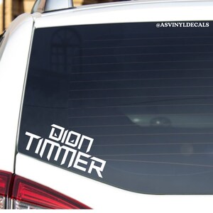 May include: White vinyl decal with the text "Dion Timmer" on a car window. The decal is in a bold, blocky font.
