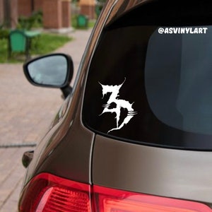 May include: A white vinyl decal with the text "3D" in a stylized font, applied to the back window of a brown car. The decal is a popular design for car customization and personalization.