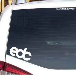 May include: White vinyl decal of the letters "edc" on a car window. The decal is on the back window of a white car. The car is parked outside. The decal is for sale on Etsy.