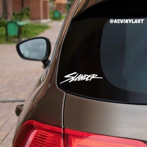 May include: A black car with a white "SLANDER" decal on the back window. The decal is in a stylized font. The social media handle "@ASVINYLART" is printed on the window above the decal.
