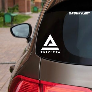 May include: White vinyl decal with a stylized triangle logo and the word "TRIVECTA" in all caps. The decal is applied to the back window of a brown car. The social media handle "@ASVINYLART" is visible in the upper right corner of the image.