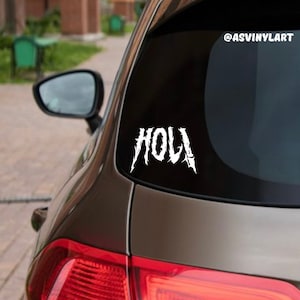 May include: A white vinyl decal with the word "HOLI" in a stylized, jagged font, applied to the back window of a brown car. The decal is on a black background. The social media handle "@ASVINYLART" is visible in the upper right corner of the image.