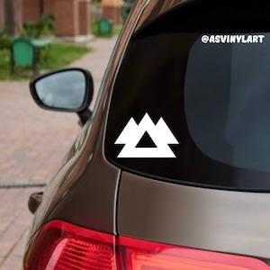 May include: White vinyl decal of a stylized mountain range design on a black car window. The decal features three triangles, with the top triangle pointing upwards and the two bottom triangles pointing downwards. The decal is placed on the back window of a car, with the text "@ASVINYLART" visible in the upper right corner of the image.