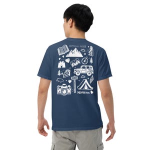 May include: Navy blue t-shirt with a white graphic design featuring camping and outdoor adventure icons, including mountains, a tent, a camera, and the text "NATIONAL PARKS" and "NOMAD1544".