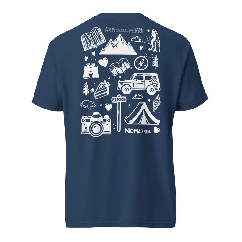 May include: Navy blue t-shirt with a white graphic design featuring camping and national park-themed illustrations. The design includes mountains, a tent, a camera, and the text "NATIONAL PARKS" and "NOMAD.JSHH".