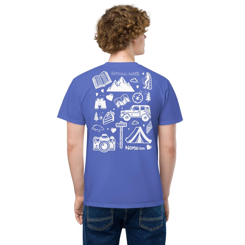 May include: A blue t-shirt with a white graphic design featuring camping and outdoor adventure icons. The design includes mountains, a tent, a camera, and the words "NATIONAL PARKS" and "NOMAD ISH".