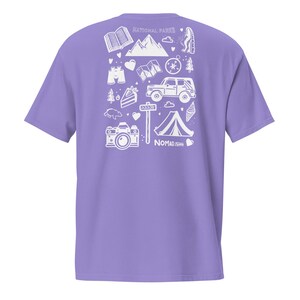 May include: A lilac t-shirt with a white graphic print of outdoor adventure icons, such as a tent, camera, and mountain range. The words "NATIONAL PARKS" and "NOMAD.ISH" are printed on the shirt.