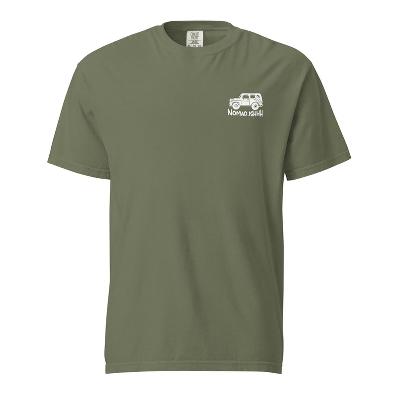 May include: Olive green short-sleeve t-shirt with a white graphic of a vehicle and the text "NOMADISHHH" on the upper right chest. The shirt has a crew neck and a relaxed fit.