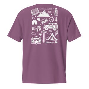 May include: Mauve t-shirt with a white graphic of outdoor adventure icons, including a mountain range, camera, tent, and compass. The text "NATIONAL PARKS" is at the top, and "NOMAD.ISH" is at the bottom.