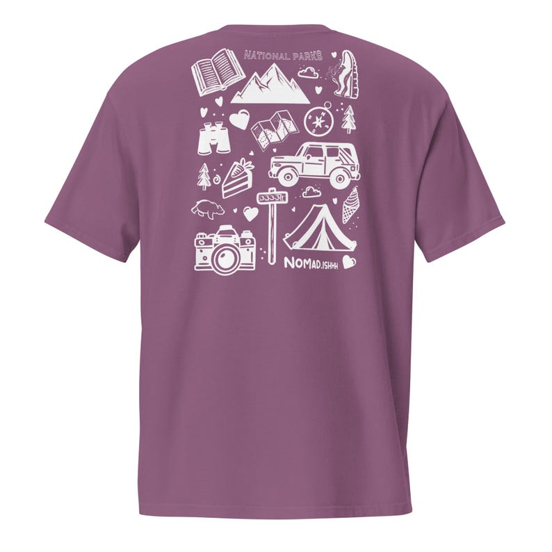 May include: Mauve t-shirt with a white graphic of outdoor adventure icons, including a mountain range, camera, tent, and compass. The text "NATIONAL PARKS" is at the top, and "NOMAD.ISH" is at the bottom.
