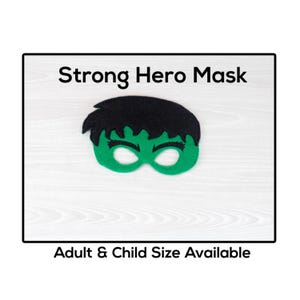 Puede incluir: Una máscara de fieltro verde con cabello negro, que se asemeja a un superhéroe. La máscara tiene agujeros para los ojos y está etiquetada como "Strong Hero Mask". El texto en la parte inferior dice "Adult & Child Size Available."