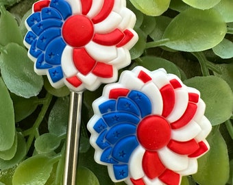 May include: Two red, white, and blue flower-shaped charms with a star pattern on the blue portion. The charms are attached to silver metal straws.