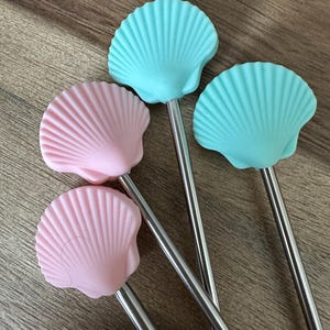 May include: Four reusable stainless steel drinking straws with silicone tips shaped like seashells. Two straws have pink seashells and two straws have light blue seashells.