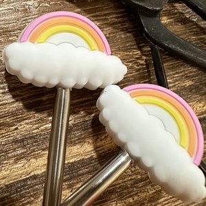 May include: Two silver stirring spoons with rainbow and cloud silicone toppers. The toppers are pink, yellow, and orange.