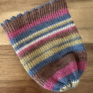 May include: A hand-knitted hat with a striped pattern in shades of brown, pink, blue, yellow, and white. The hat has a scalloped edge and a rounded shape, suitable for cold weather. The hat is made of soft yarn.