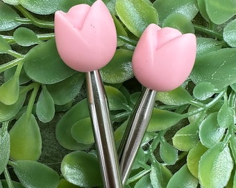 Puede incluir: Dos agujas de tejer de color rosa en forma de tulipán con ejes de metal plateado.