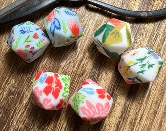 May include: Six colorful, floral patterned, geometric dice. The dice are made of a white material and have a variety of floral patterns in shades of blue, red, green, and yellow.