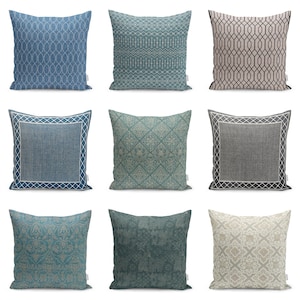 May include: A collection of nine square throw pillows featuring various patterns including geometric lines, damask motifs, and bordered designs in shades of blue, teal, gray, and beige. Each pillow has a small white fabric tag on the side.
