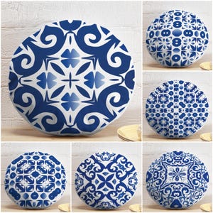 Può includere: Cuscini decorativi rotondi con motivi blu e bianchi. I cuscini presentano vari disegni geometrici e floreali, offrendo una gamma di stili. I cuscini sono disposti su una superficie di legno contro un muro di mattoni bianchi.